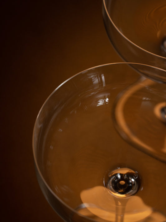 Close-up of two clear Fable coupe glasses lit warmly against a dark amber background