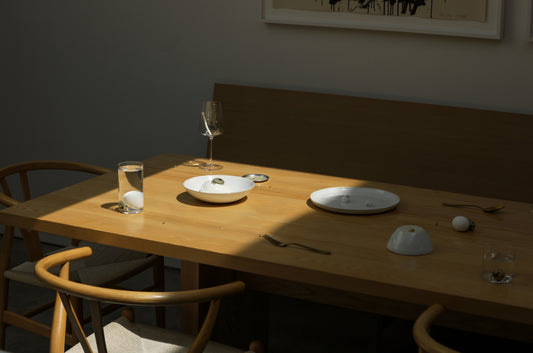 Sunlit wooden dining table set with Fable pearl white dinnerware, glassware and wine glass beside wooden chairs