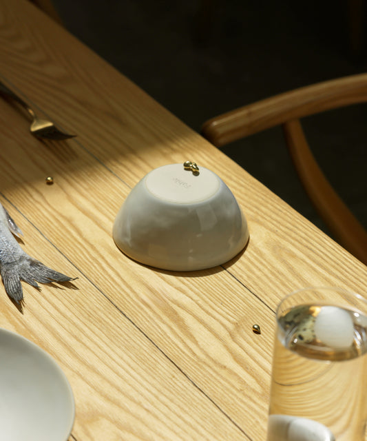 Pearl White Fable bowl upturned on a sunlit ash wood table with a wine glass and fish in a styled scene