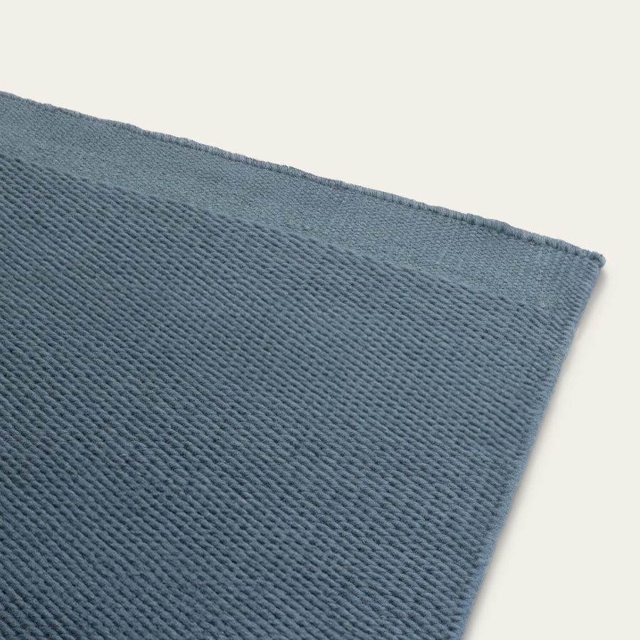 Close-up of a textured blue rug on a light gray background. #seasideblue