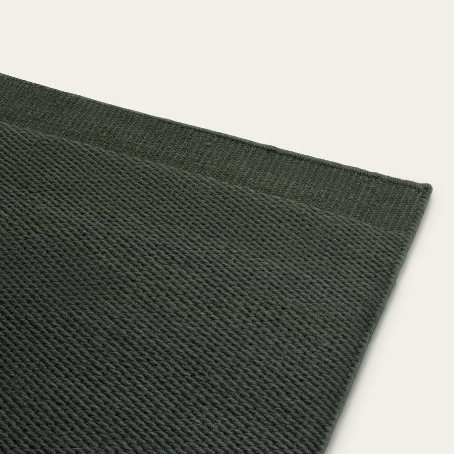 Close-up of a dark green woven rug corner on a light gray background #forestgreen