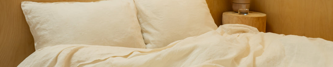 Bed made with cream linen bedding and pillows against a wooden headboard