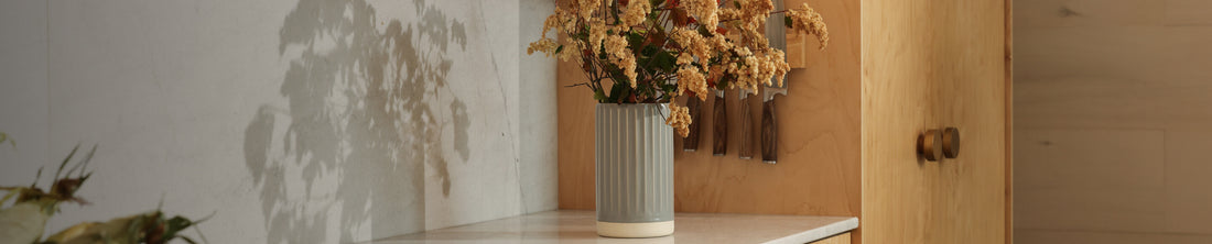 Grey ribbed ceramic vase filled with dried yellow flowers on a kitchen countertop