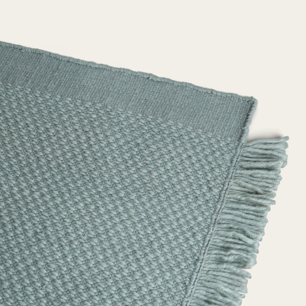 Textured teal blanket with frayed edge on a light gray background #sagegreen