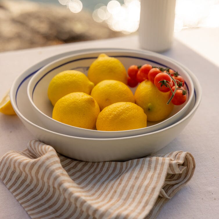 Bowl of lemons and cherry tomatoes on a table with a striped cloth and blurred natural background