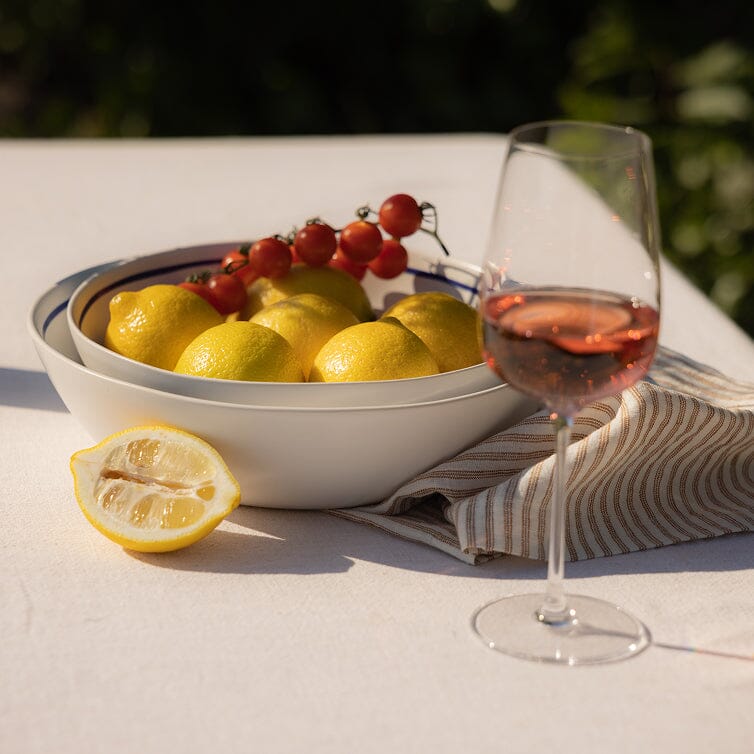 Bowl of lemons and tomatoes with a glass of pink wine on a table outdoors.