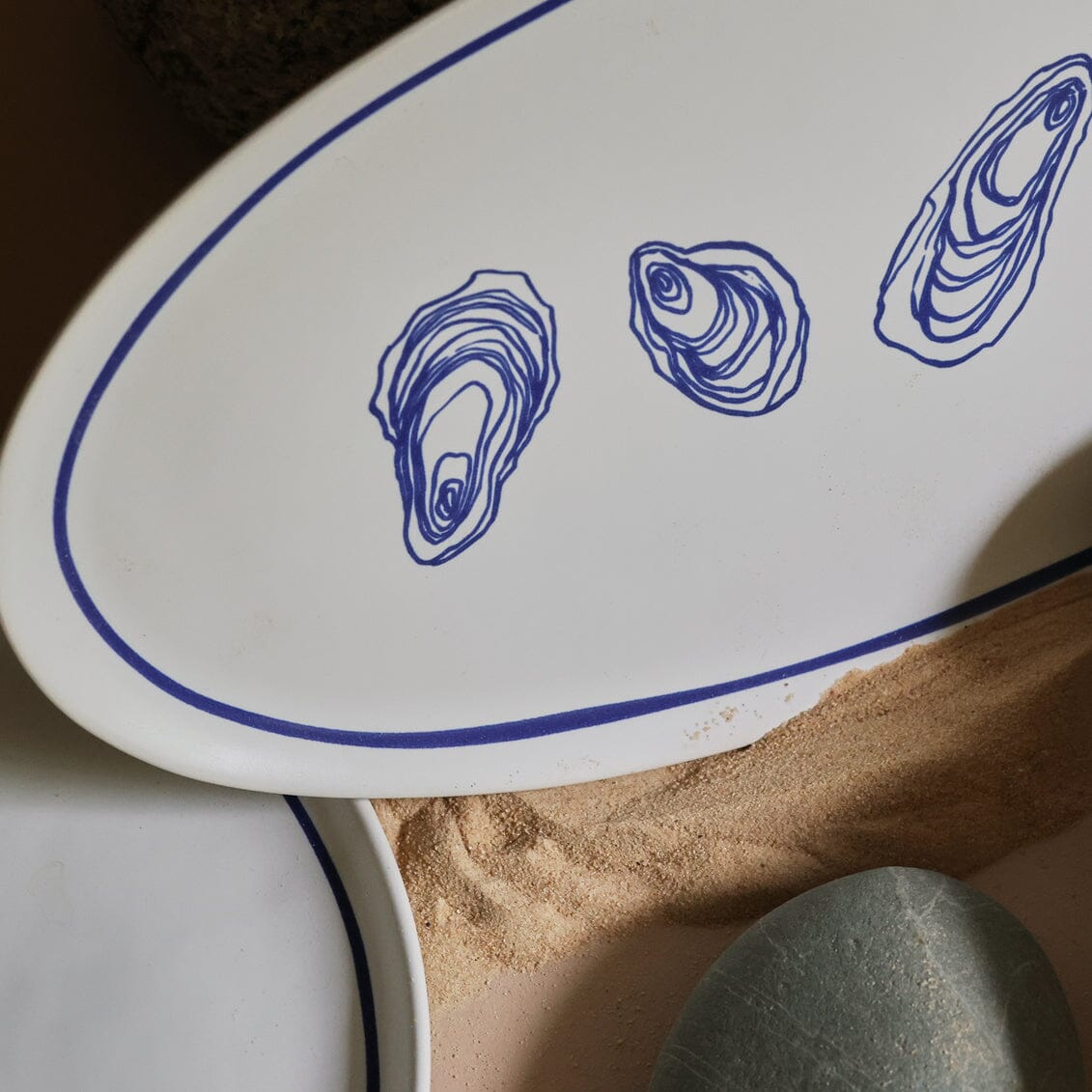 Close-up of a white paddle with blue oyster illustrations on a sandy surface.