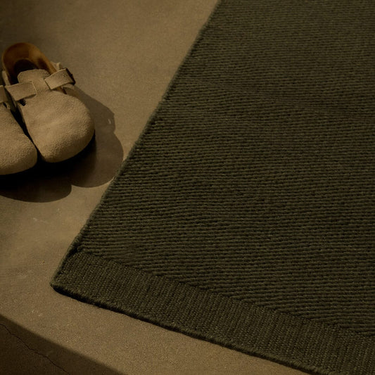 Brown shoes on a concrete surface next to a green textured rug. #forestgreen