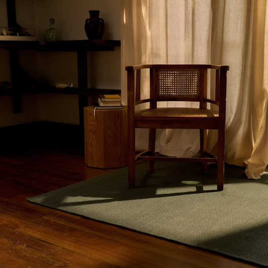 Wooden chair with wicker backrest in a dimly lit room with curtains and a shoreline green rug. #forestgreen
